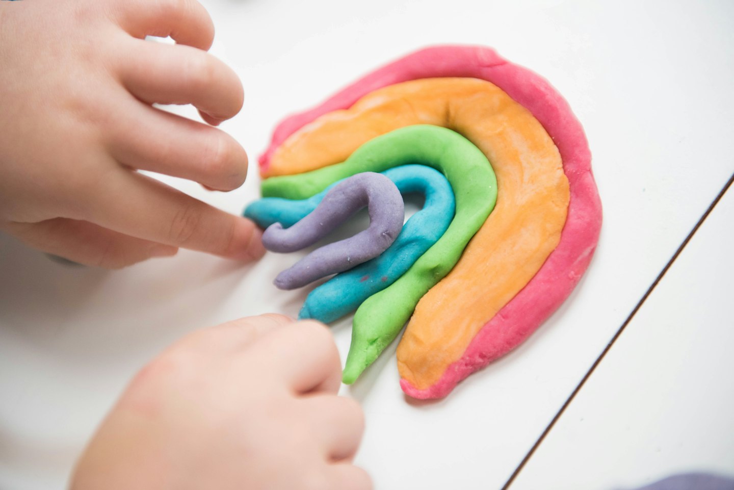 Child's hands shaping colorful play-doh into a rainbow.
