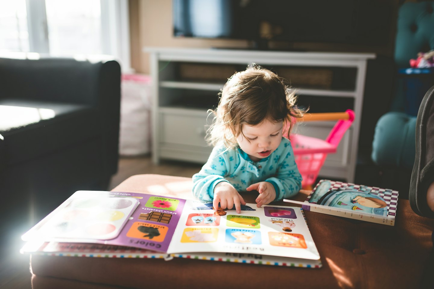 Toddler pointing at a colorful board book on a sofa.