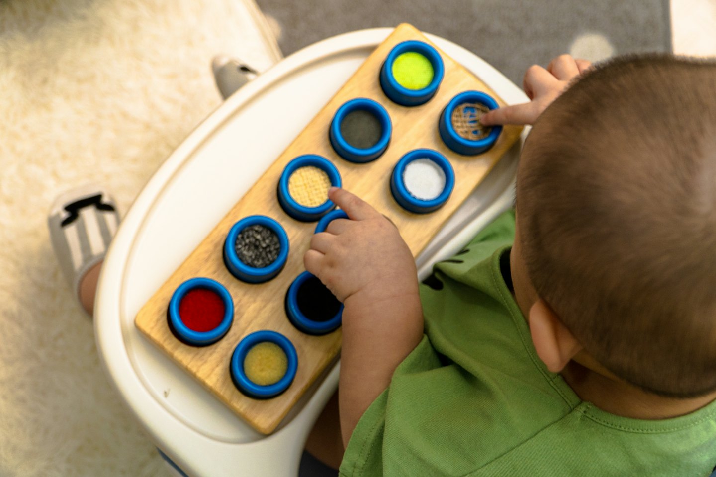 Toddler in a high chair playing with a sensory board.