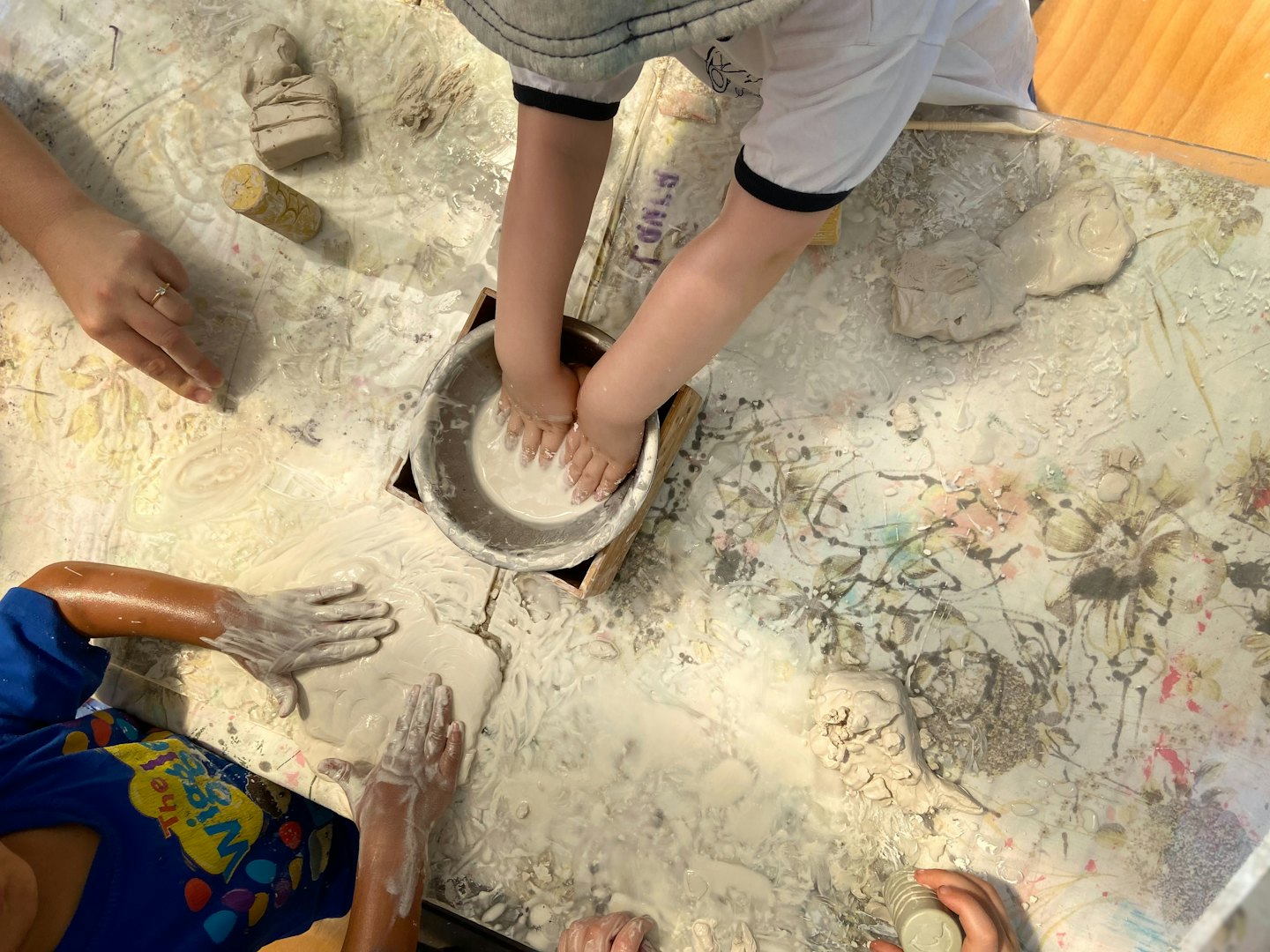 Two children and an adult play with clay on a table.