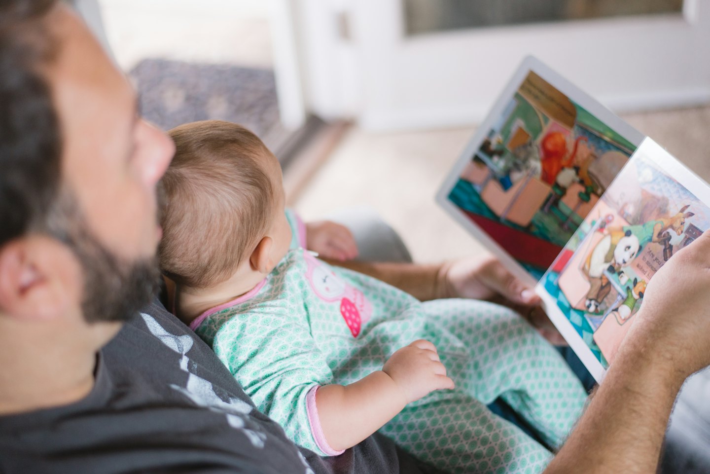 Bearded man reads a colorful picture book to a baby.